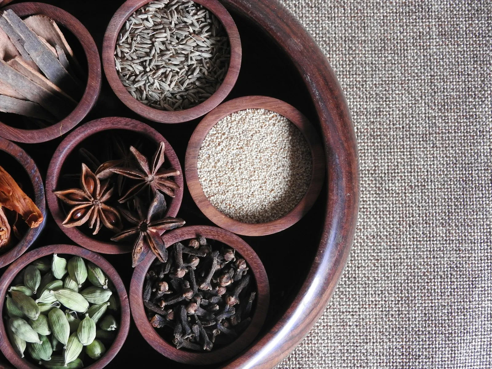 Traditional round spice box with small bowls of cumin, cloves, star anise, cardamom and other whole spices