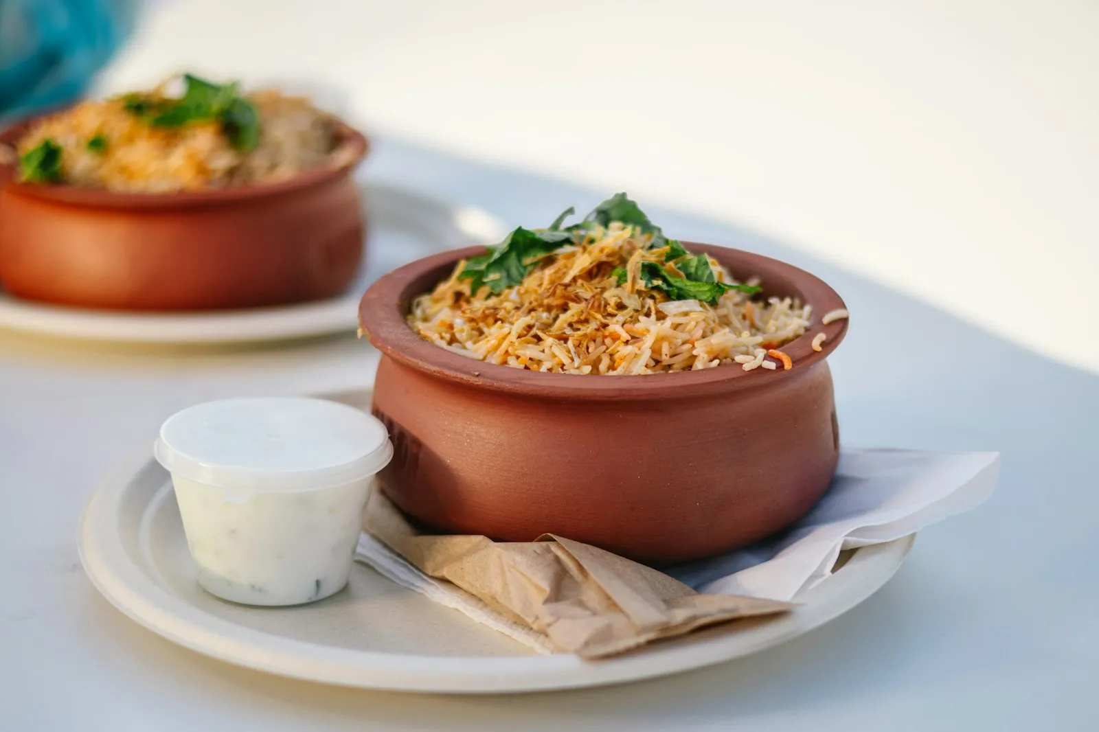 Biryani served in a clay pot with a cup of raita on the side