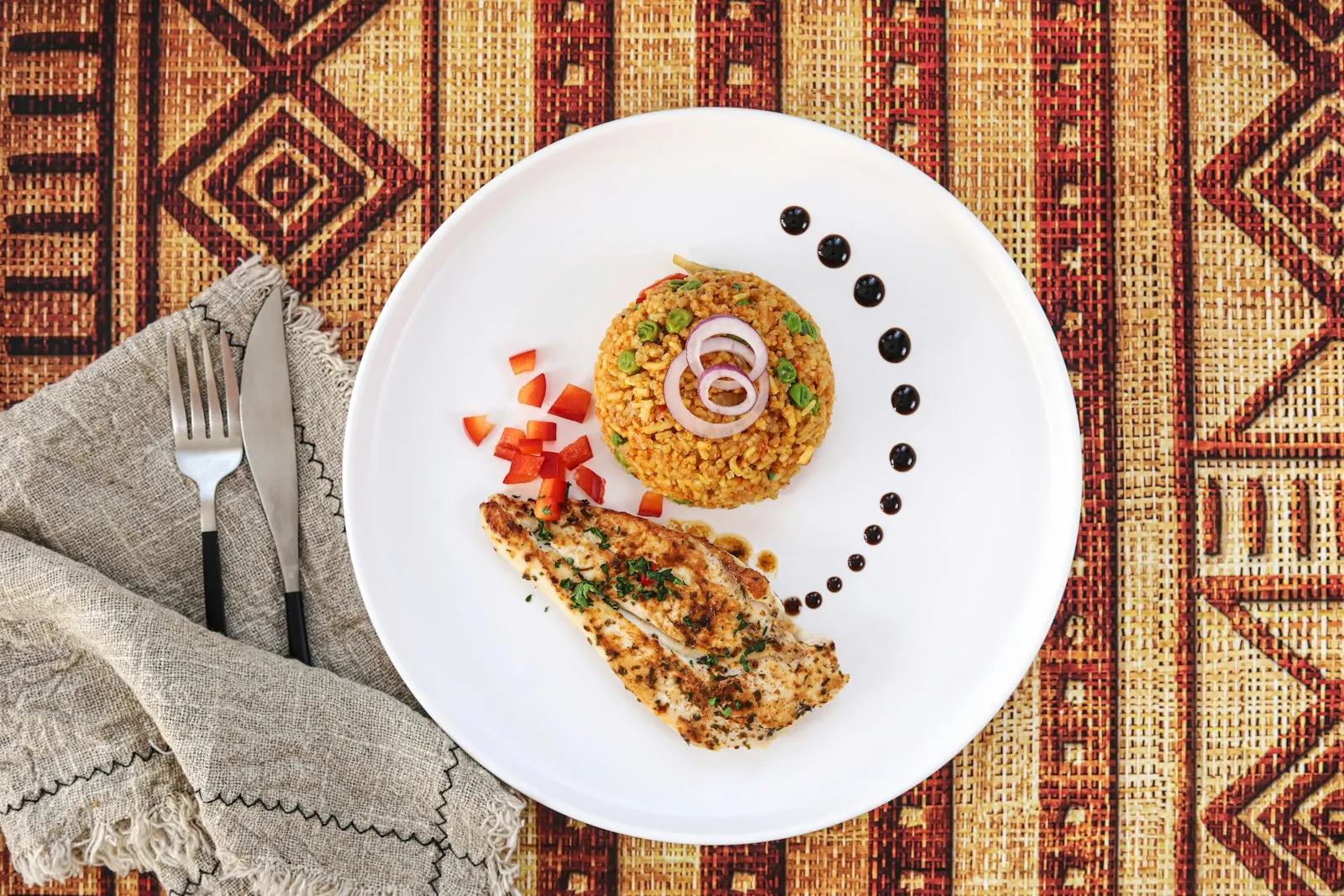 Plated jollof rice with grilled chicken breast and red onion on a patterned mat