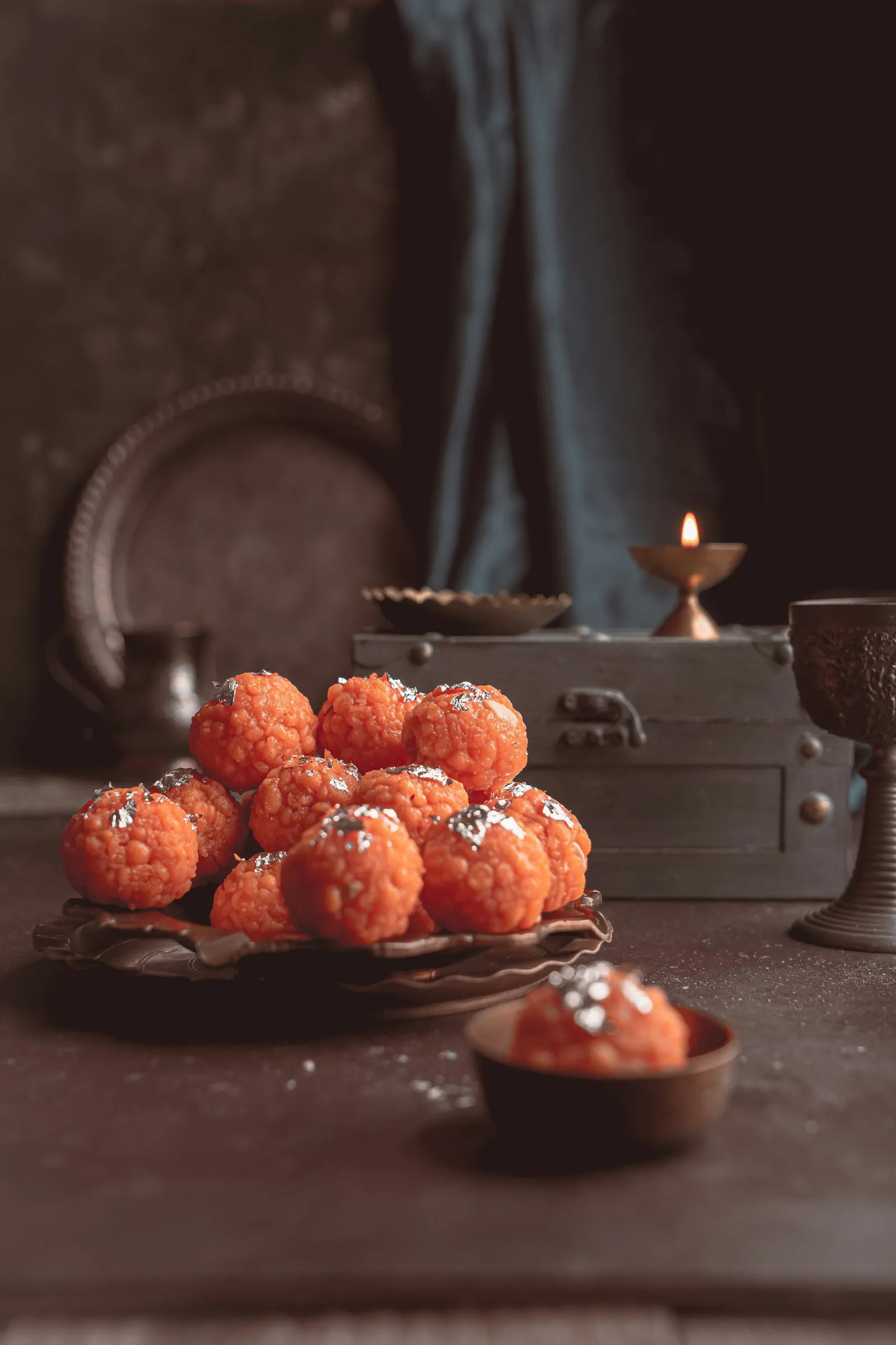 Plate of boondi laddoos beside a small lit oil lamp in warm low light