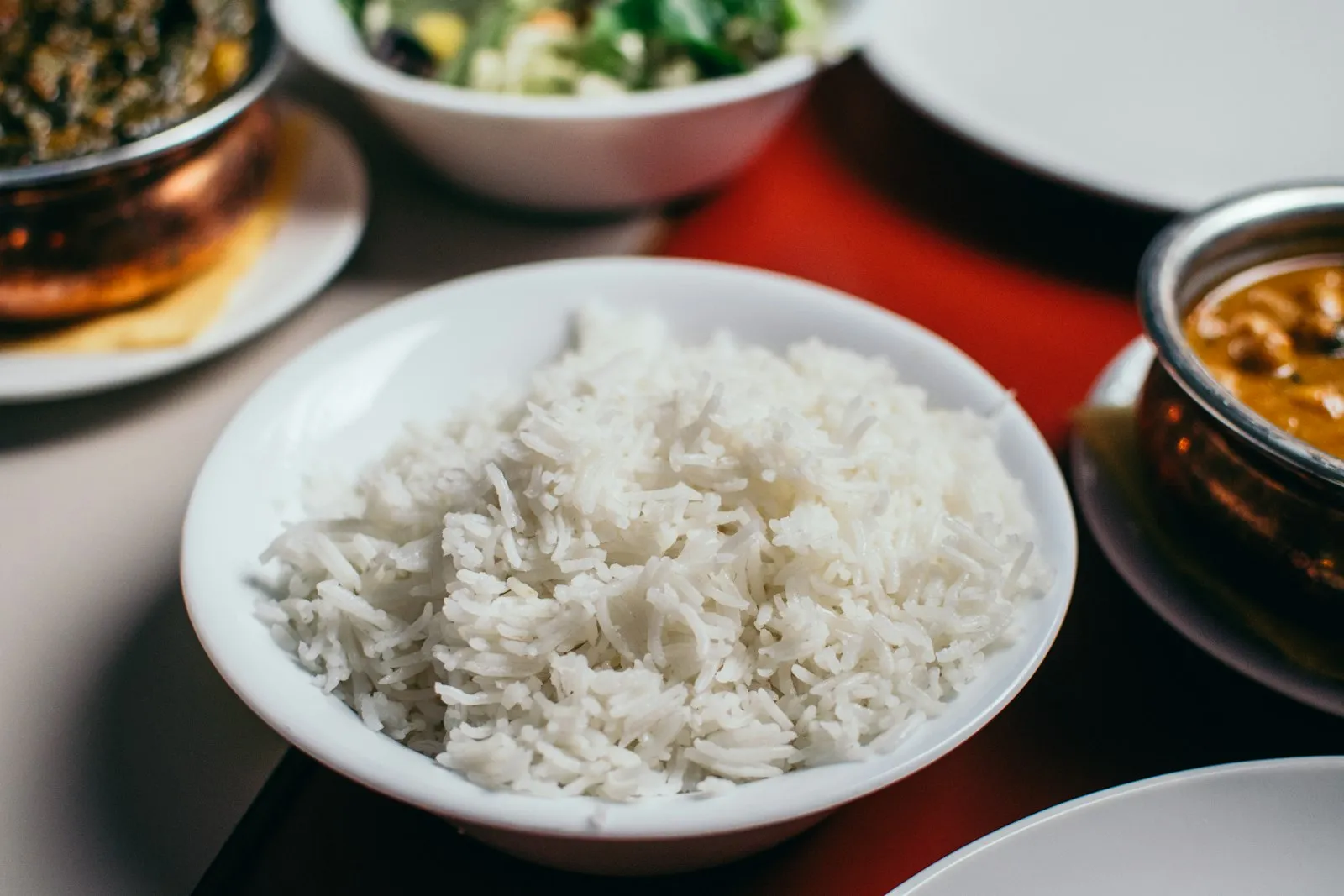White bowl of plain steamed rice with side dishes blurred in the background