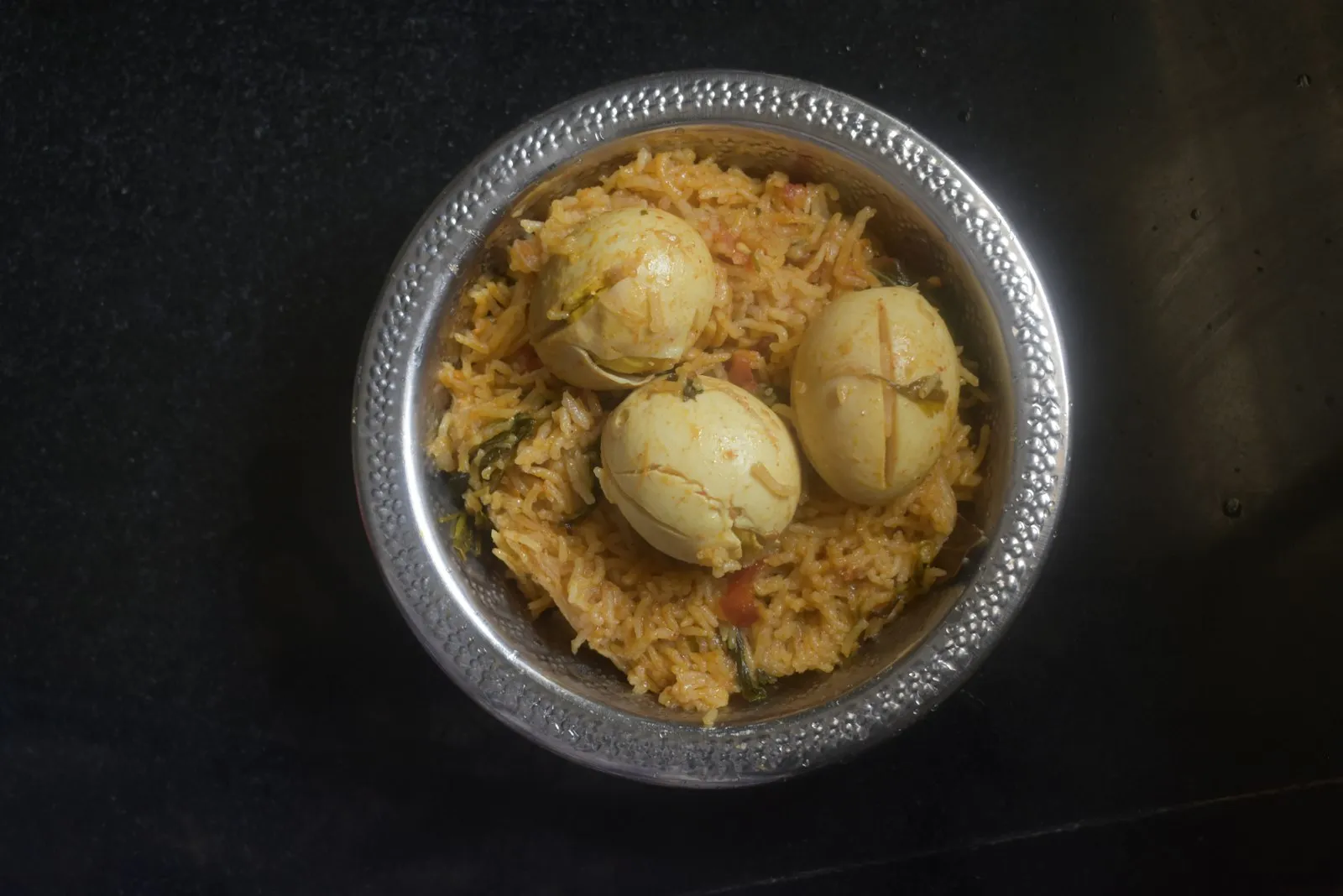 Steel bowl of egg biryani with whole boiled eggs nestled in spiced rice