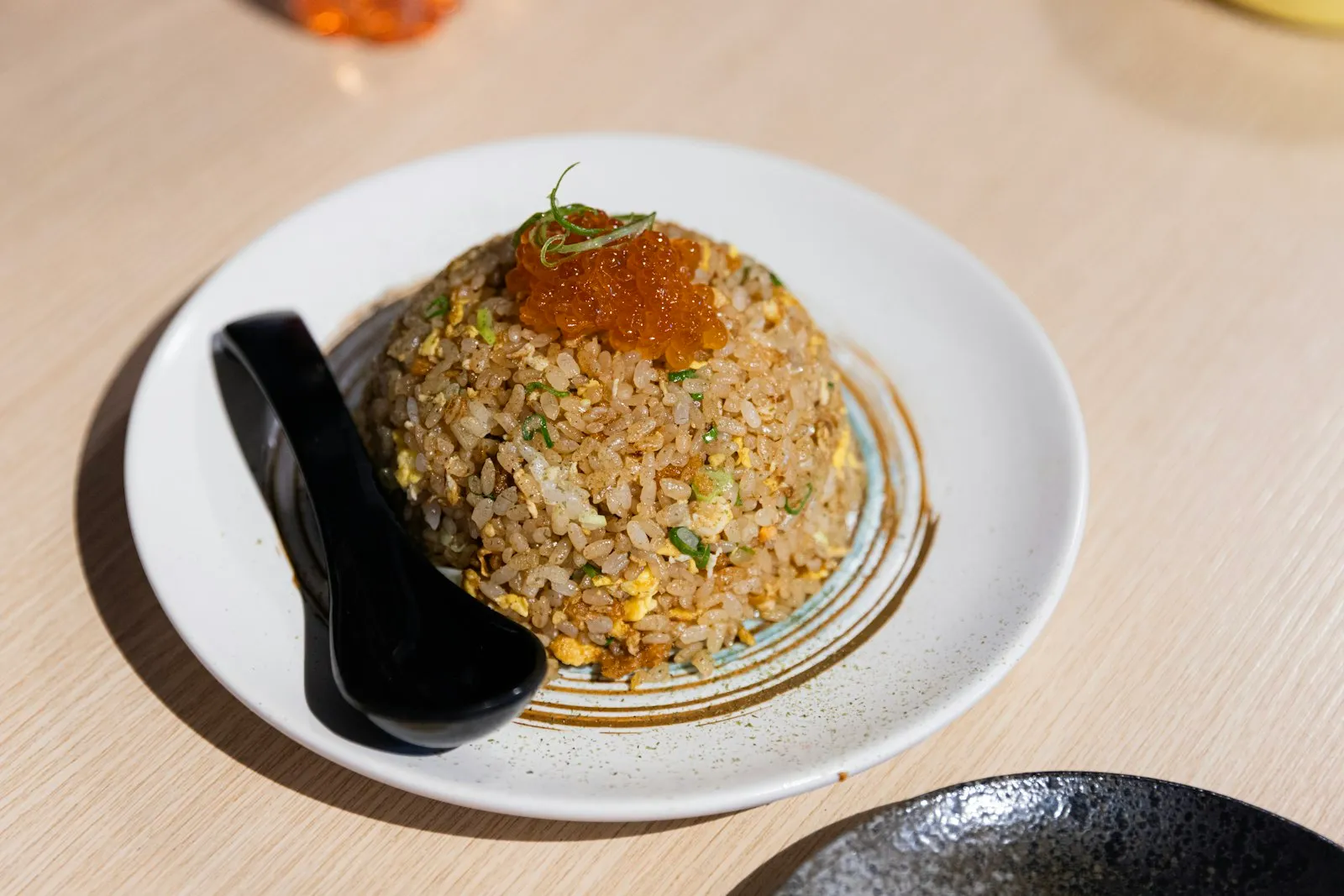 Dome of Japanese-style fried rice topped with roe on a white plate with a black spoon