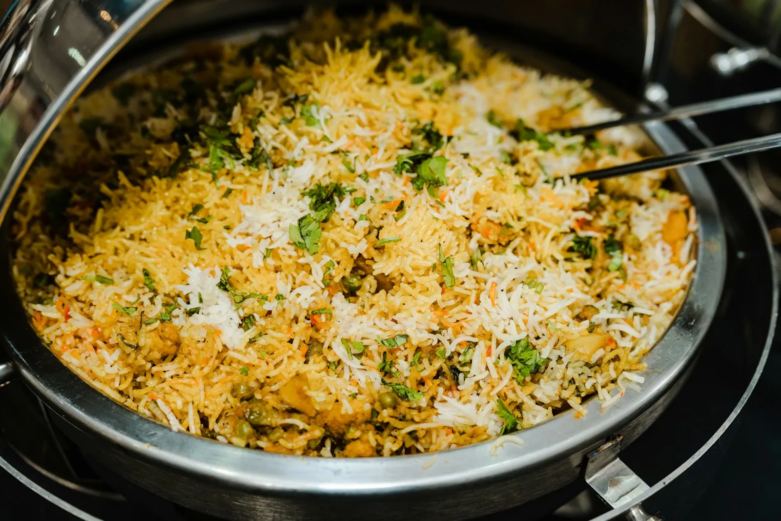 Stainless steel pan filled with layered yellow and white biryani rice and herbs