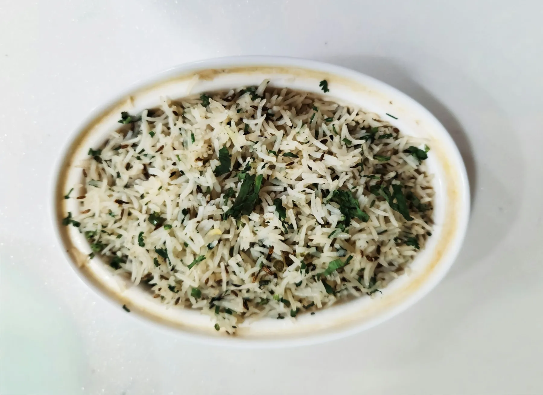 White oval dish of basmati rice flecked with cumin seeds and chopped cilantro