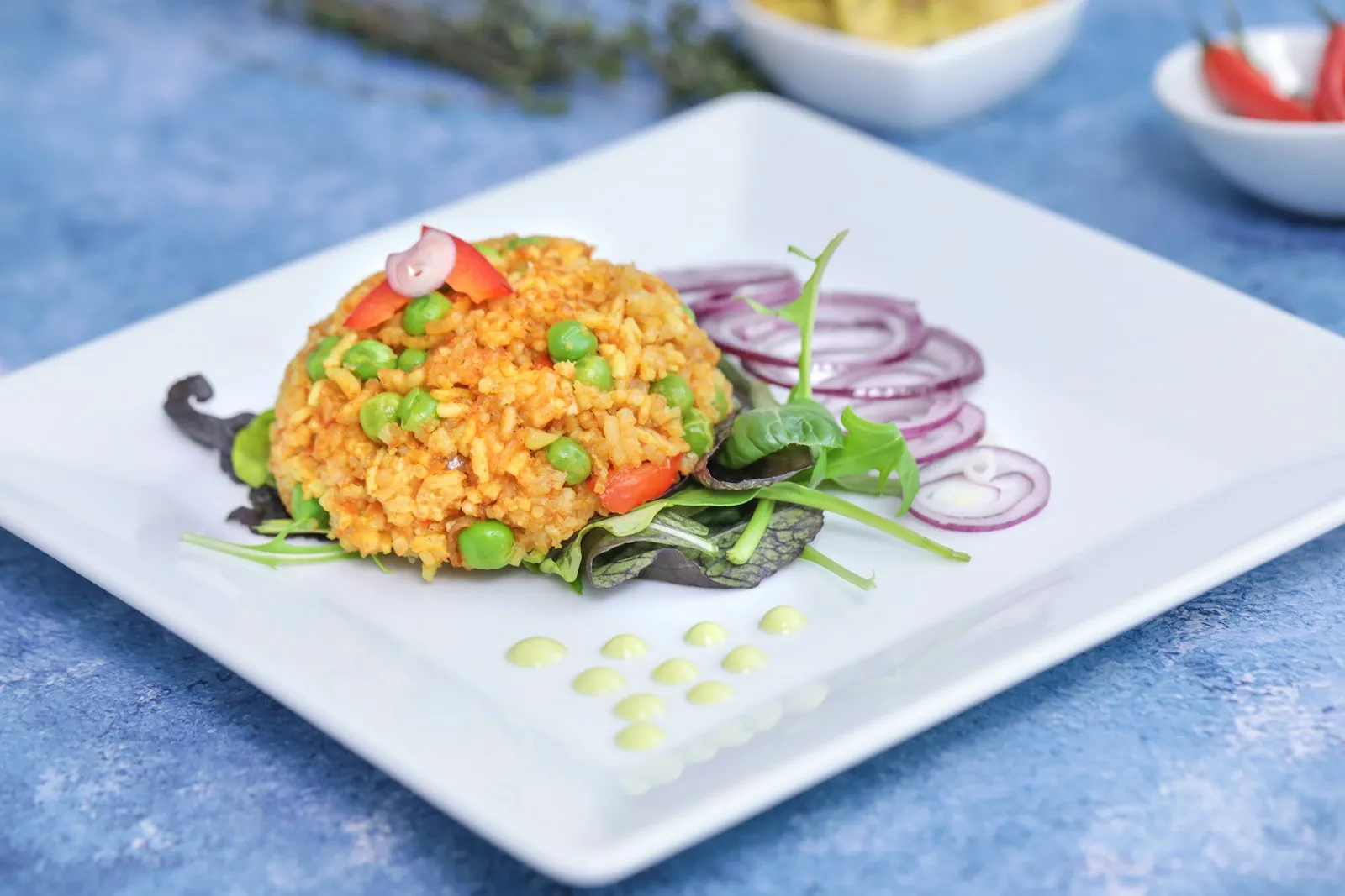 Mound of jollof rice with peas and red onion rings on a white square plate