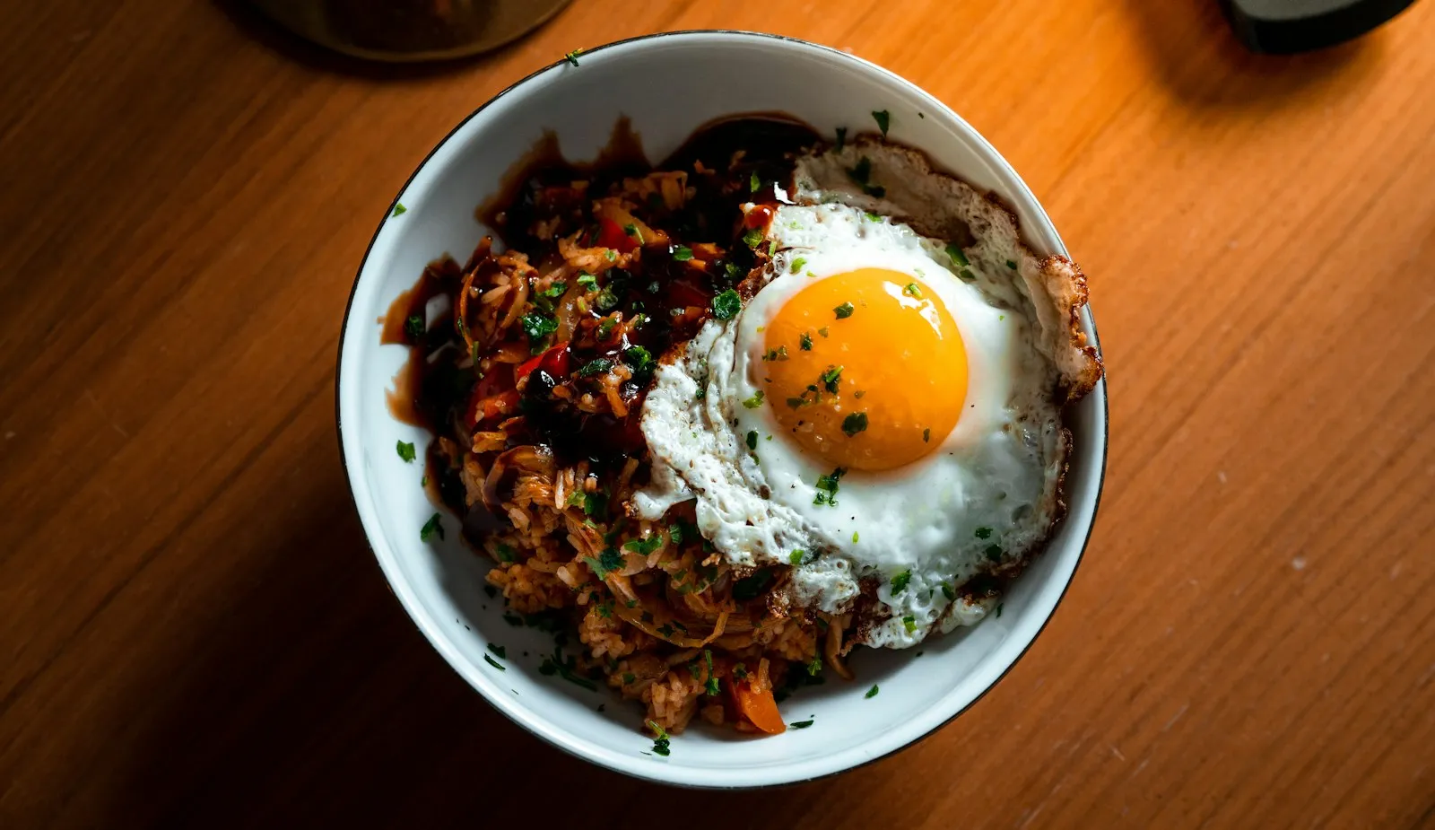White bowl of kimchi fried rice topped with a sunny-side-up egg on a wooden table