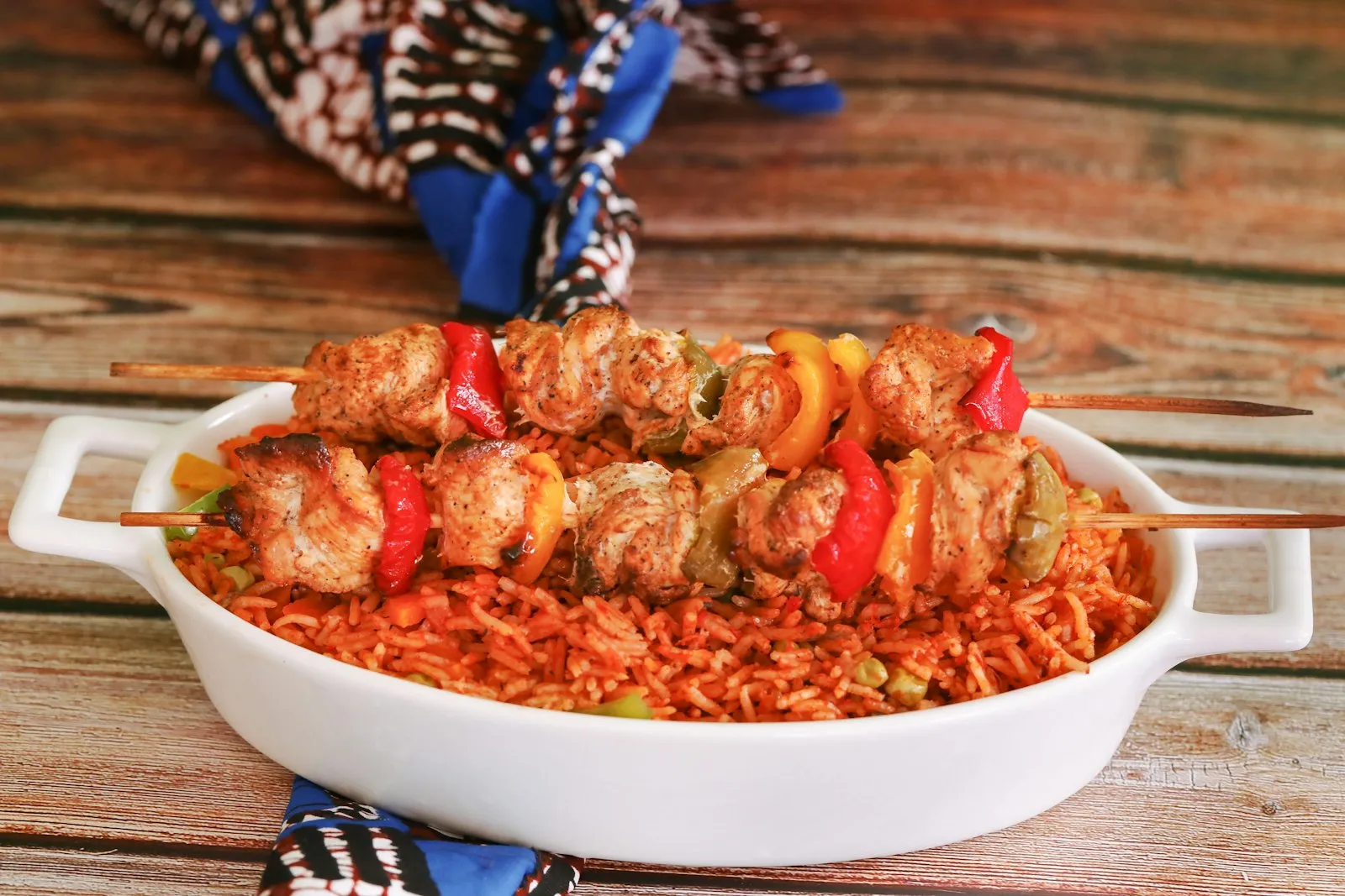 Oval dish of Nigerian jollof rice topped with chicken and pepper skewers
