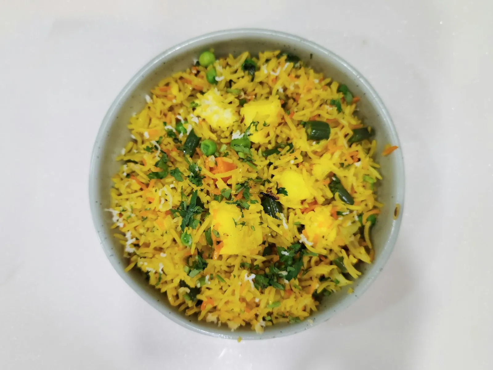 Bowl of yellow spiced rice with peas, carrots and soft cubes of paneer
