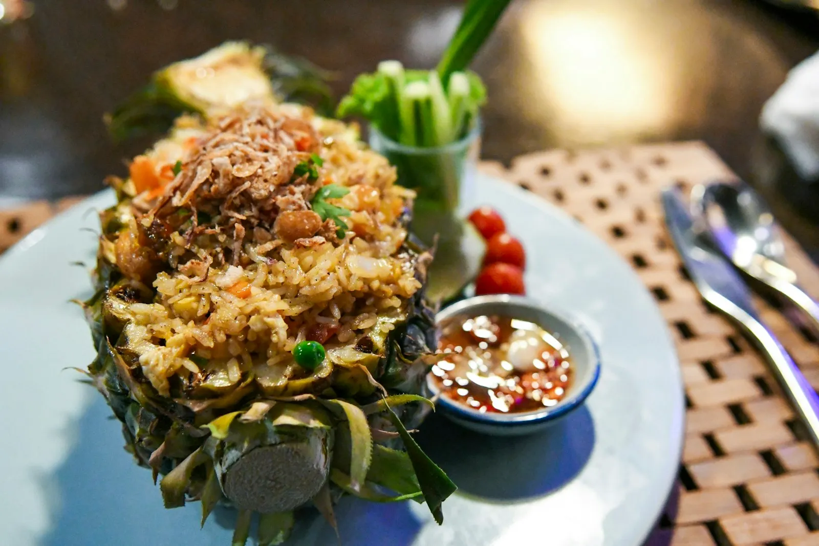 Fried rice served in a hollowed pineapple half with a dipping sauce and fresh vegetables