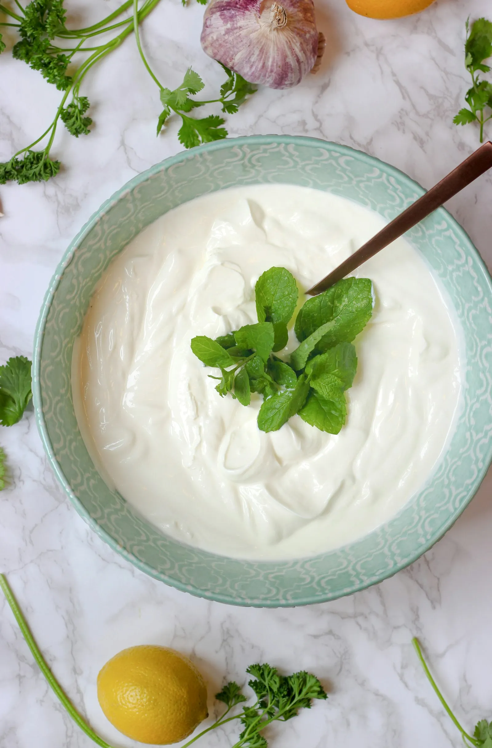 Bowl of thick yogurt garnished with fresh herbs, with a wooden spoon
