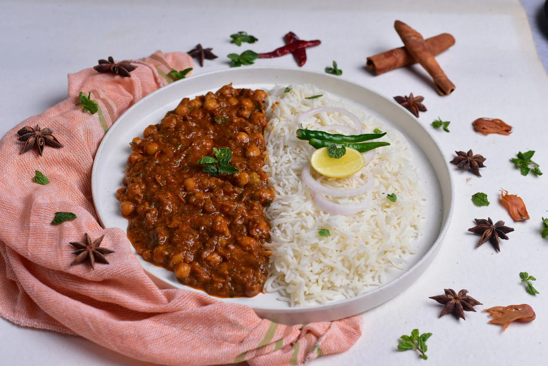 Teal plate of kidney bean curry around a mound of cumin rice, garnished with mint and tomato, with chutney and butter behind