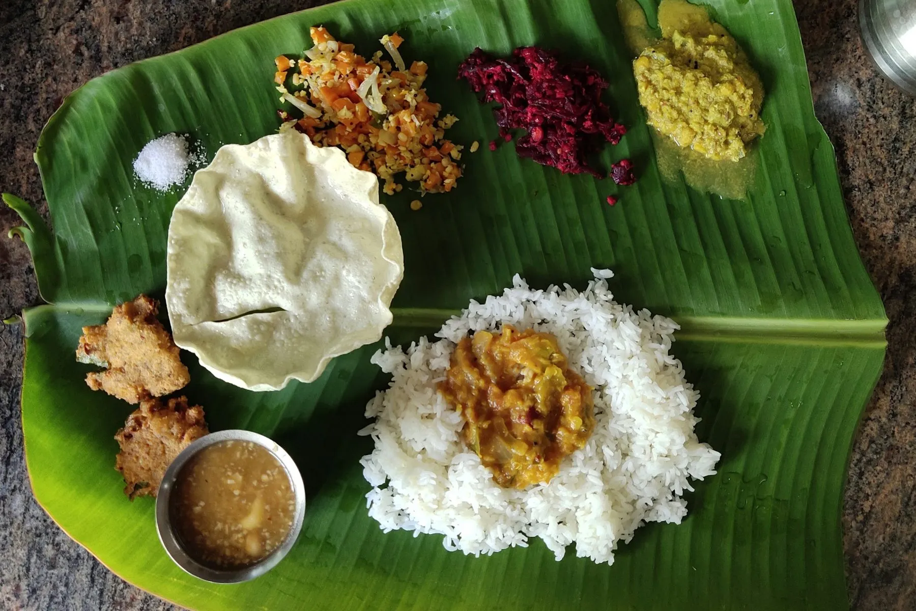Banana leaf meal of rice topped with dal, with papad, vadas, vegetable sides and a cup of rasam