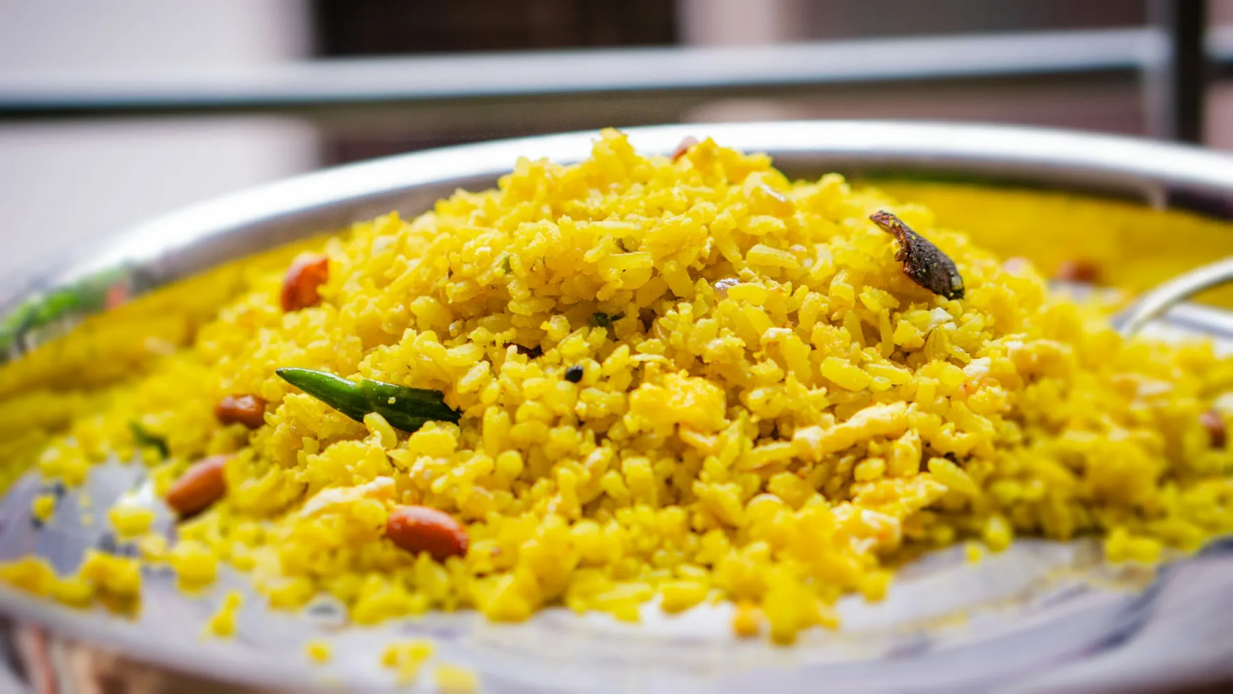 Plate piled with yellow tempered rice with peanuts, curry leaves and a dried chili