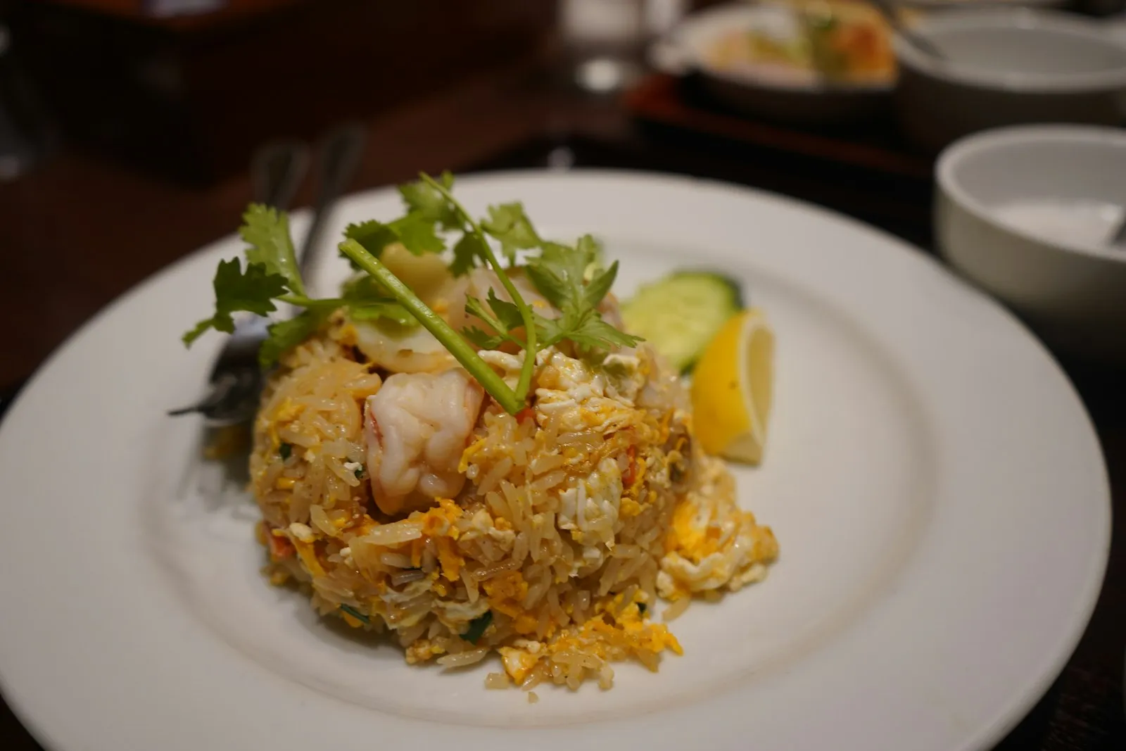Plate of Thai-style fried rice with shrimp, lime wedge, cucumber and herbs