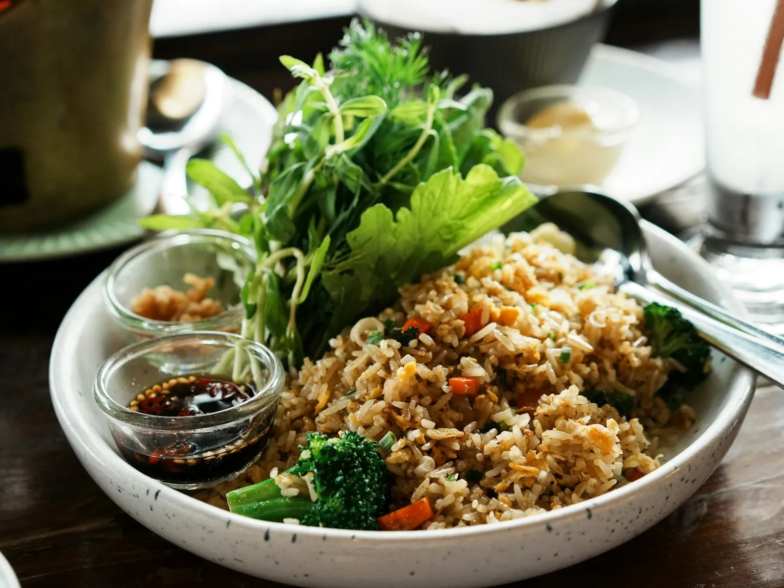 Bowl of vegetable fried rice with broccoli, carrots and fresh greens, with a small dish of soy sauce