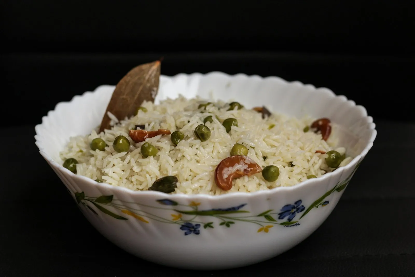 Floral bowl of green peas pulao with whole spices on a dark background